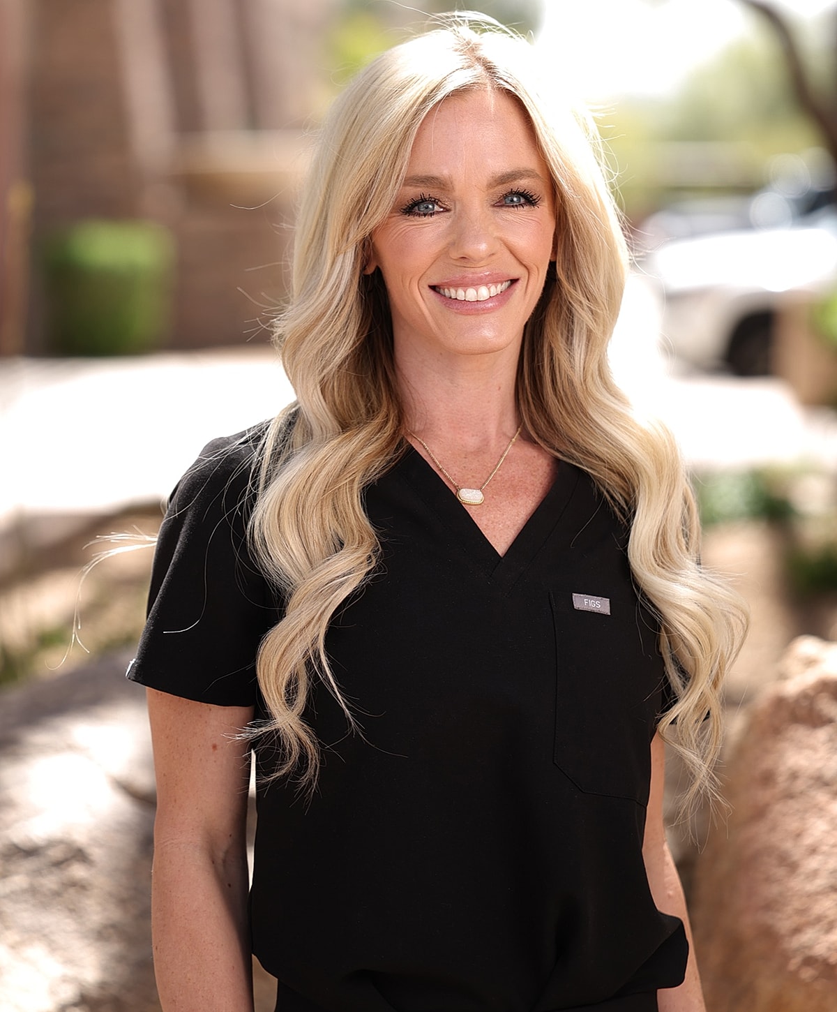 Smiling woman in black scrubs outdoors.