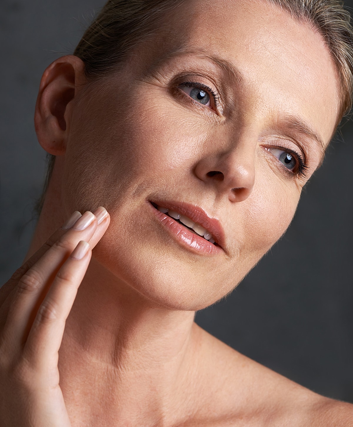 Woman with gray hair gently touching her face.