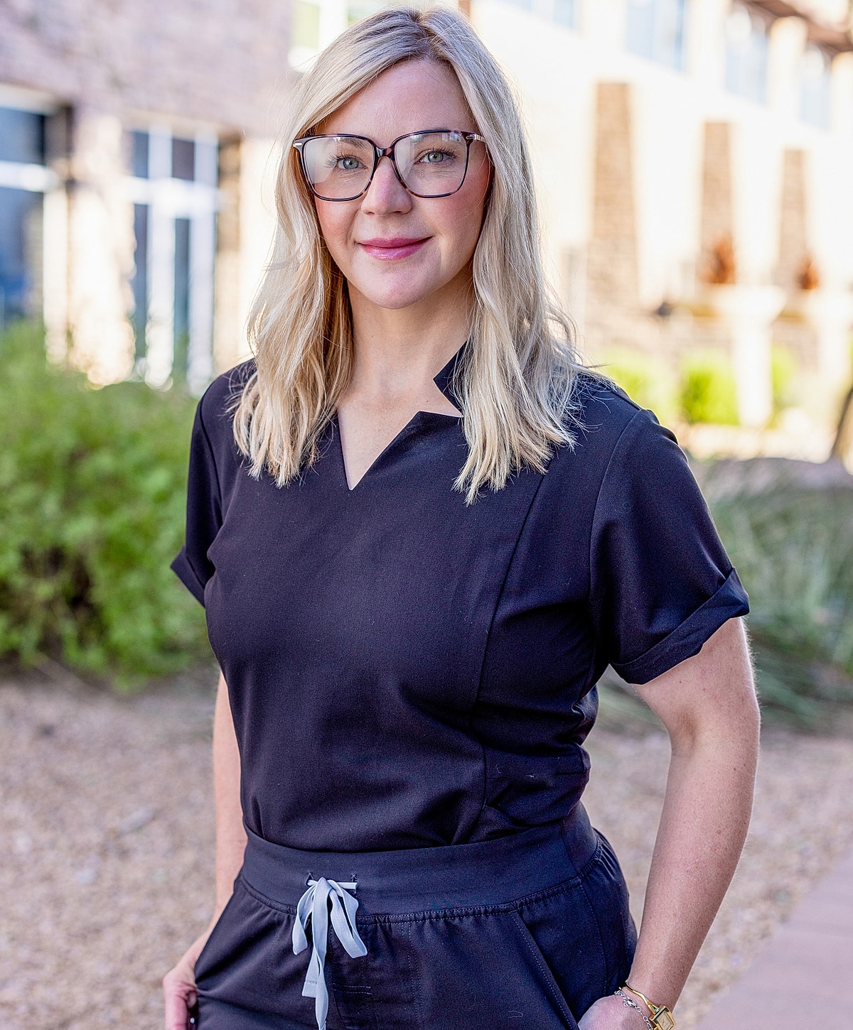 Woman in black outfit with glasses outdoors.