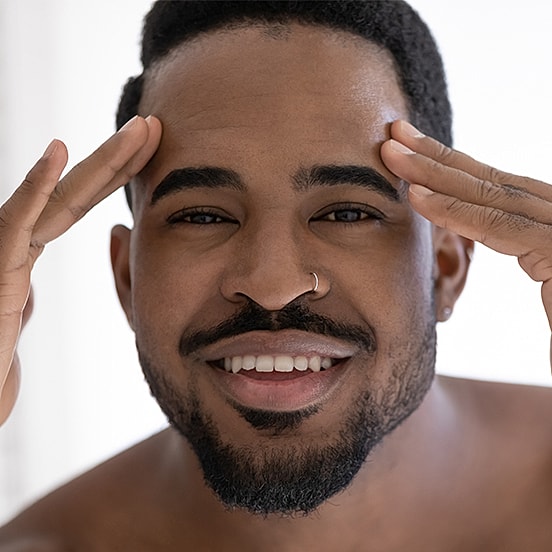 Smiling man touching his forehead, joyful expression.