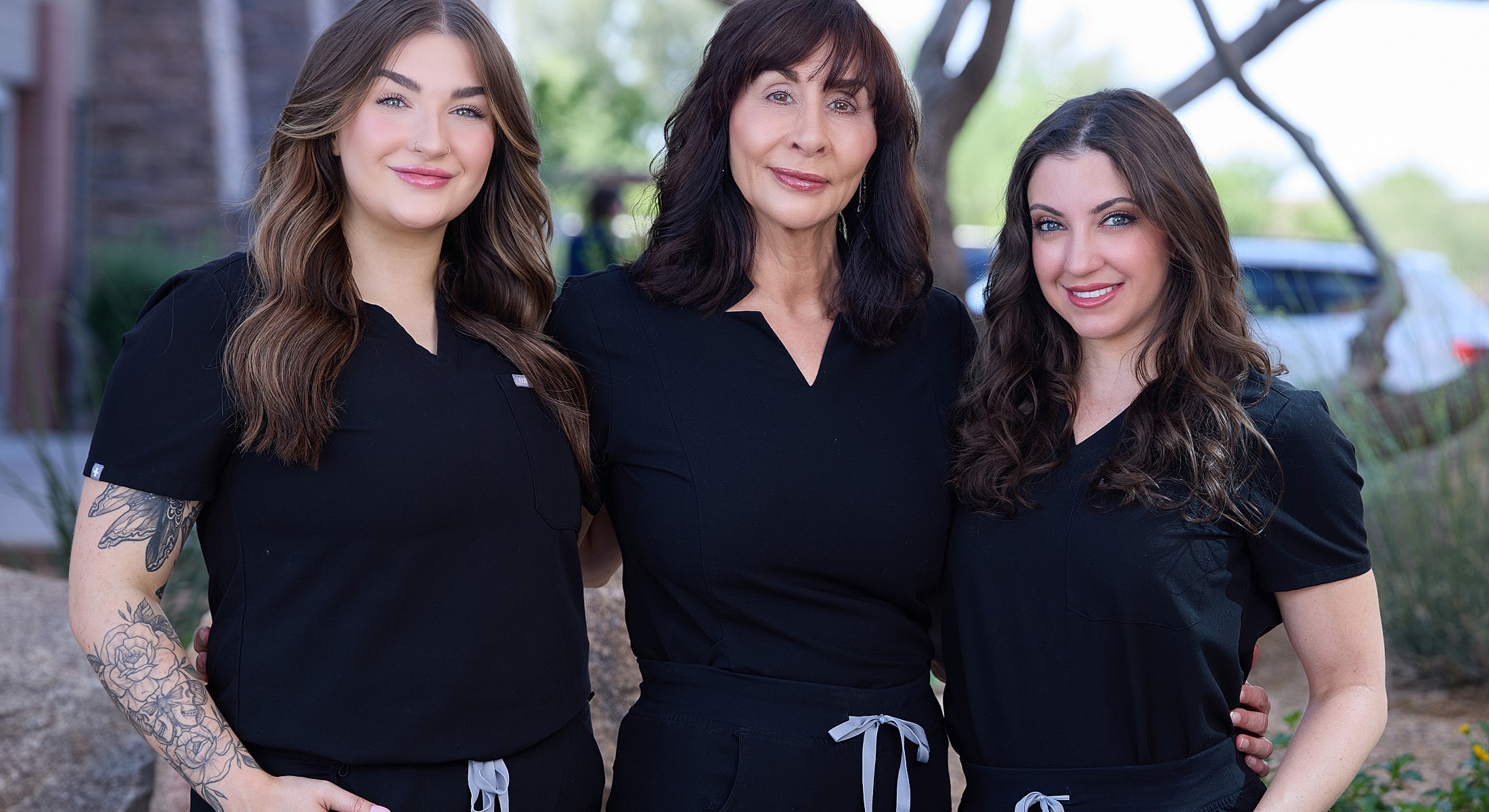 Three women in scrubs smiling outdoors.