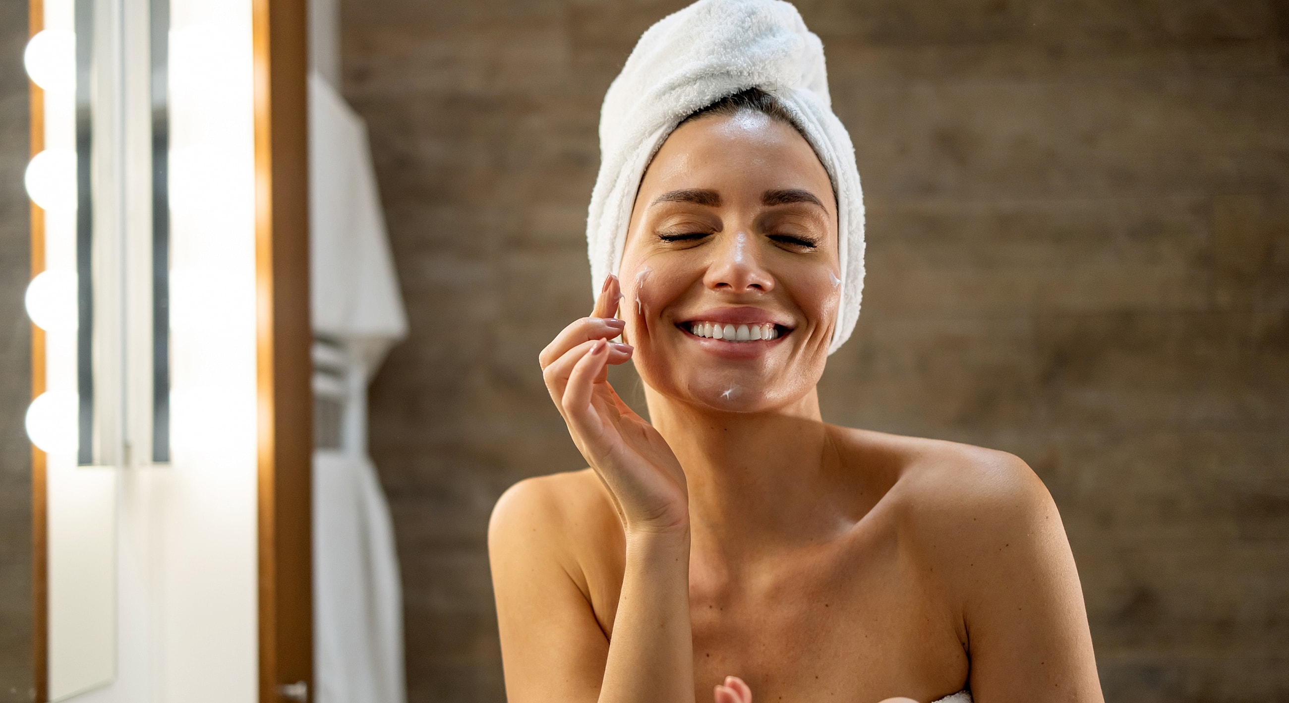 Woman smiling while applying skincare product.